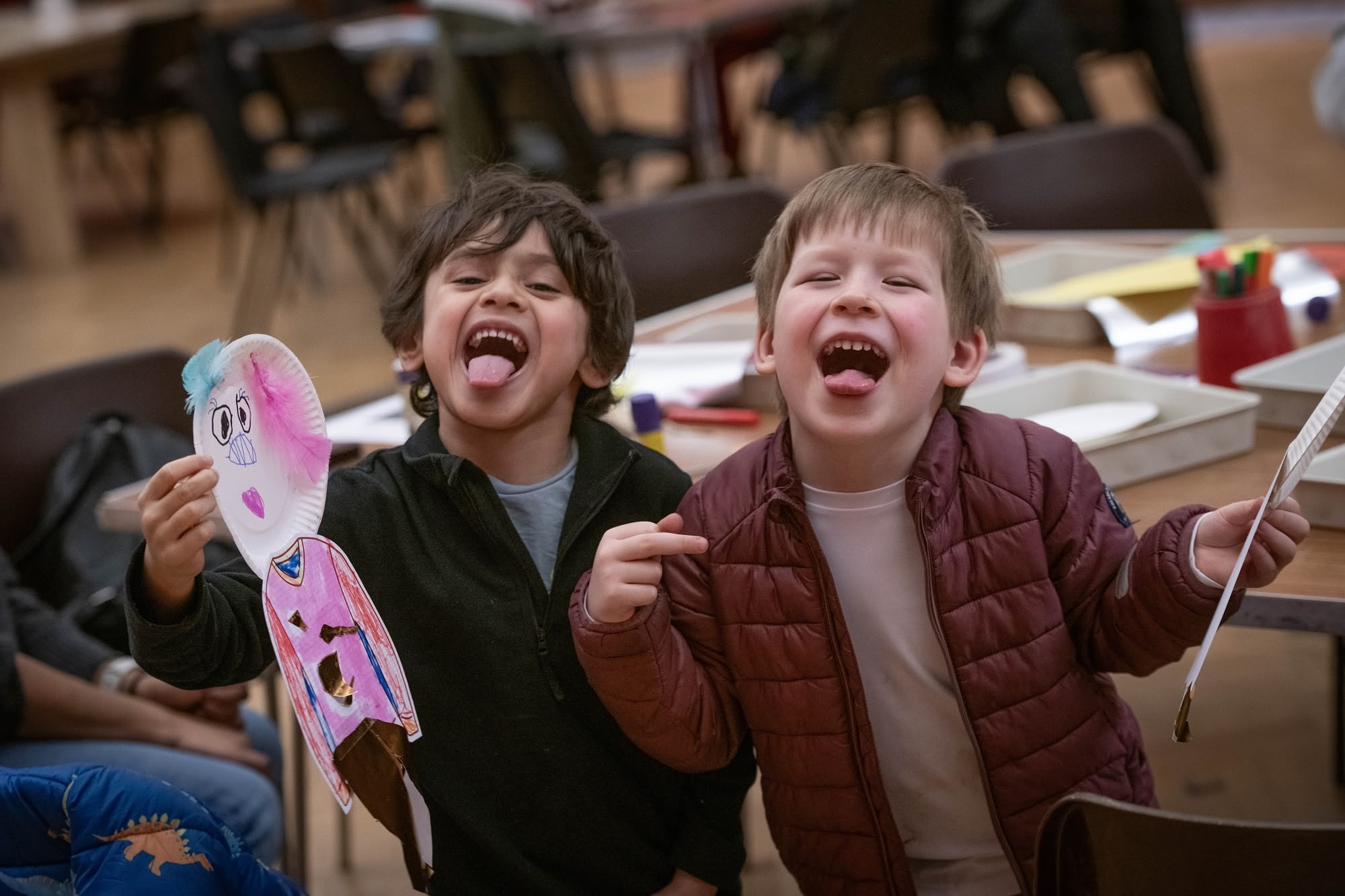 Two children at a crafting session. Both sticking their tongues out at the camera.