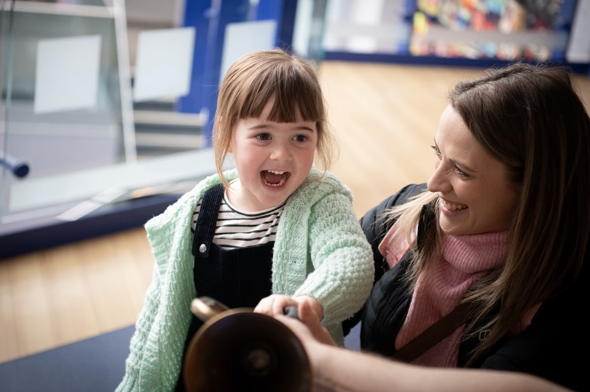 A young child and her mother enjoying playing with a brass instrument