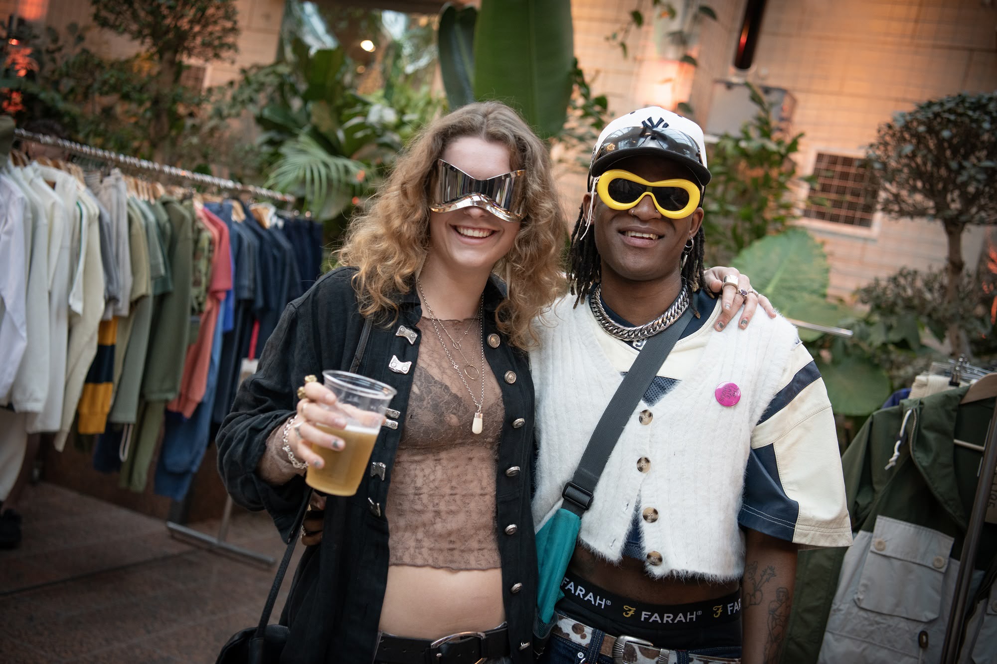 Two attendees of The Late Shows wearing futuristic sunglasses, surrounced by clothes racks