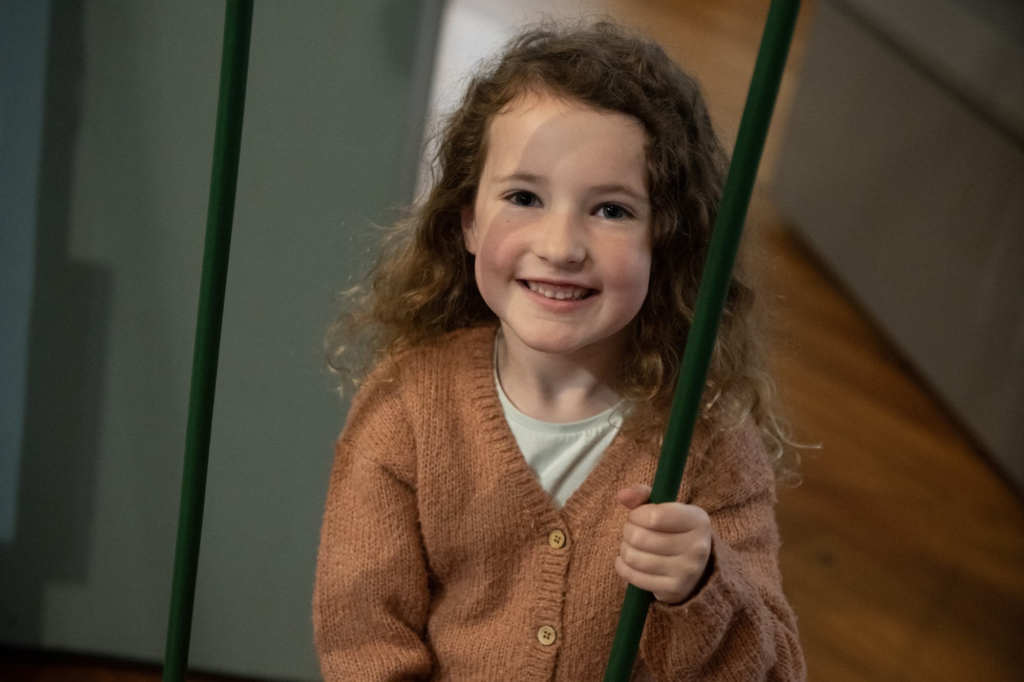 Smiling child with curley brown hair and brown cardigan.